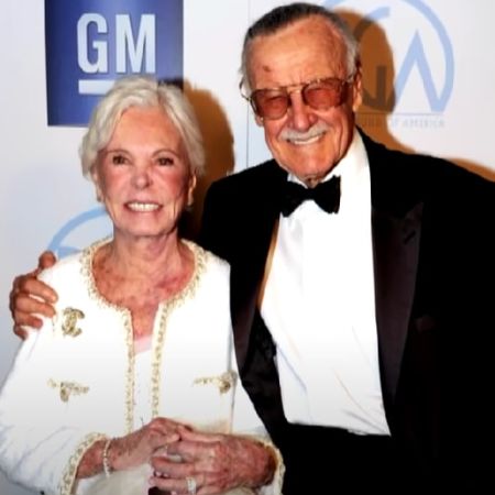 Stan Lee is wearing a tuxedo and Joan Boocock Lee is wearing a white dress. 